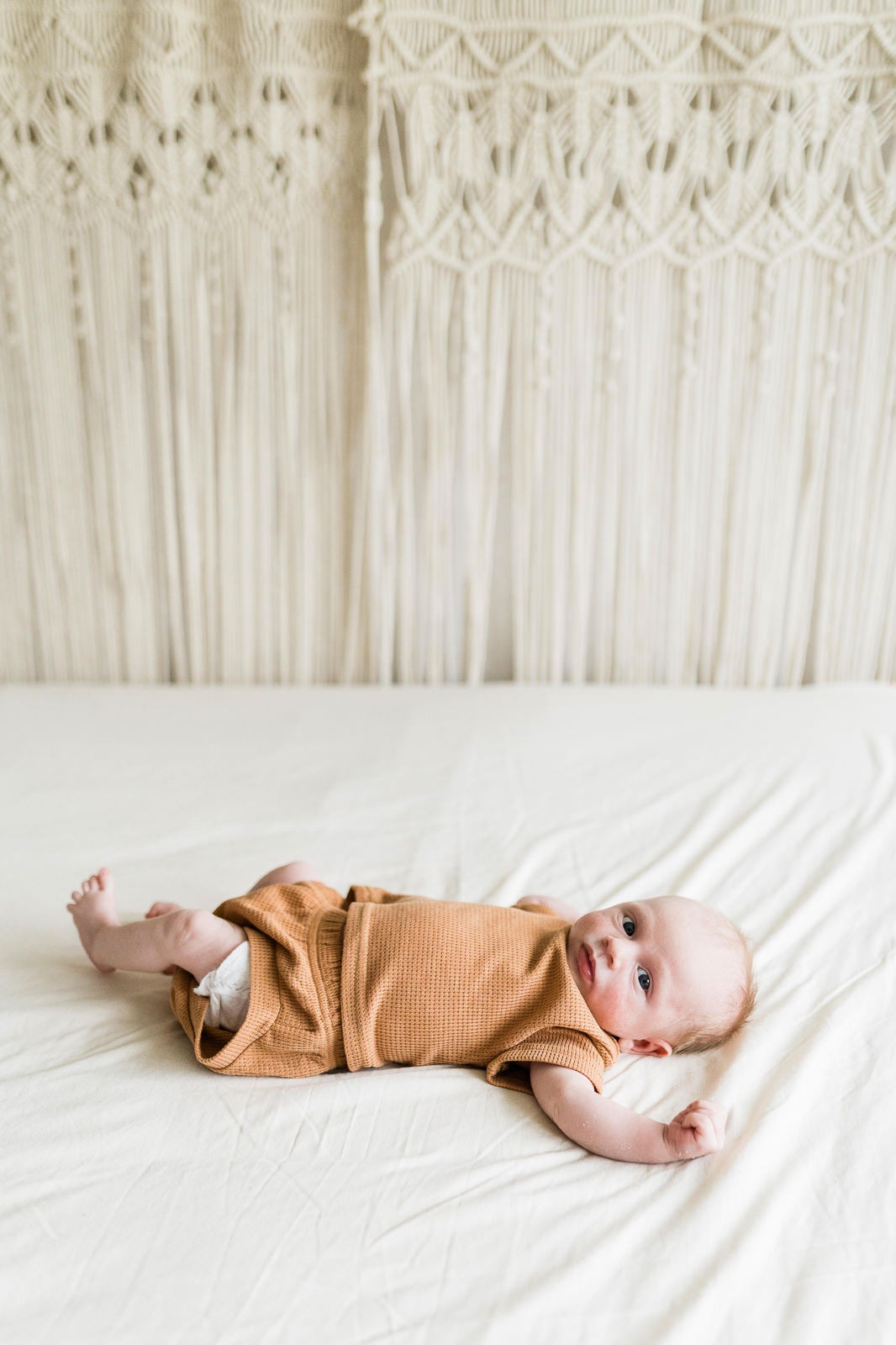 photo de bébé en tenue couleur rouille et fond macramé